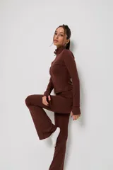 Conjunto deportivo de dos piezas color marrón, compuesto por una campera de cuello alto con cierre frontal y mangas largas con abertura para pulgar, y un pantalón de corte ajustado con terminación acampanada.