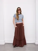 Falda larga color marrón, de corte amplio y fluido, con cintura elástica fruncida, bolsillos laterales y detalle de volado horizontal en la parte inferior.