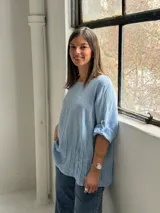Blusa celeste de corte holgado, con cuello redondo, mangas tres cuartos con trabilla y detalles de alforzas en el frente.