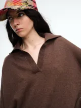 Sweater de punto color verde oliva, con cuello polo abierto en V, manga larga con hombros caídos y terminaciones acanaladas en puños y ruedo.