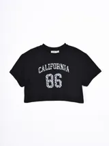 Remera crop top negra de manga corta con dobladillo en las mangas. Presenta un estampado frontal con la palabra CALIFORNIA y el número 86 en un diseño de animal print gris.