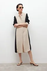 Vestido camisero midi de lino, color beige con paneles laterales en negro, cuello camisero, cierre frontal con botones y mangas largas con puños abotonados.