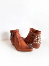 Botas de caña corta de cuero terracota, con taco cuadrado y punta fina. Cuentan con doble cierre lateral con tiradores metálicos y detalles de apliques texturizados en la parte trasera.
