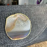 Sobre de fiesta tipo clutch, tejido artesanalmente en la India con rafia color negro grisáceo y aplique de piedra ágata natural con borde dorado. Incluye asa de cadena dorada para colgar al hombro.