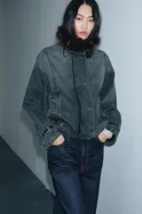 Chaqueta tipo bomber de denim lavado azul, corte holgado, con cuello solapa y aplicación de pelo sintético marrón desmontable. Presenta bolsillos delanteros y bajo acabado en elástico.