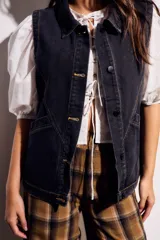 Chaleco oversize de denim negro con costuras en hilo ocre, cuello camisero, cierre frontal con botones y bolsillos delanteros.