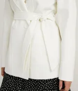 Campera alargada de polivelour color blanco, con cuello alto que se pliega y se ata a la cintura, mangas largas, abotonado frontal doble, bolsillos y cinturón.