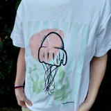Remera blanca de algodón con estampa frontal ilustrada en tonos celestes y rosados, de corte holgado y mangas cortas.