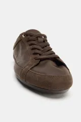Zapatilla estilo blucher con diseño deportivo, confeccionada en una combinación de materiales textiles y gamuza en tono marrón, con detalle de contraste en color blanco en el talón y cierre mediante cordones.