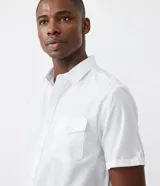 Camisa de hombre de manga corta color marrón, confeccionada en lino y algodón. Presenta cuello clásico, botonadura frontal, bolsillo en el pecho y mangas con botón para enrollar.