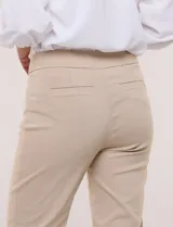Pantalón de gabardina elastizada color beige, de tiro medio y calce slim. Cuenta con diseño pull-on sin cierres ni botones, cintura ancha, bolsillos delanteros simulados y bolsillos traseros ojal.