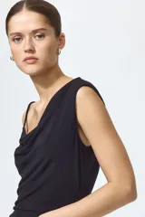 Vestido midi negro confeccionado en punto de crepé, de corte ajustado con escote asimétrico, un bretel fino y un hombro drapeado. Presenta frunces laterales que generan un efecto drapeado en la cintura y largo hasta la rodilla.
