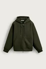 Canguro relaxed fit de tejido técnico con elasticidad efecto neopreno, color verde militar, con capucha ajustable, cierre frontal de cremallera de doble dirección, bolsillos frontales tipo canguro y acabados en rib.