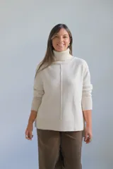 Sweater de punto color crudo con cuello alto, manga larga y detalle de costura vertical central. Presenta puños y ruedo acanalados.