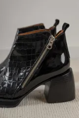 Botinetas de cuero con textura reptil en color bordó, con cierre lateral metálico y taco cuadrado de madera en tono natural.