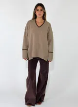 Sweater de punto azul marino con cuello en V, mangas largas con puños acanalados y detalle de línea en color marrón en el cuello y puños. Presenta un pequeño aplique decorativo en la parte inferior.