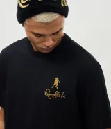 Remera de algodón color negro con cuello redondo y mangas cortas. Presenta una estampa de gran tamaño en la espalda que ilustra a Ronaldinho con un balón sobre la cabeza y el número 10, acompañada por el texto 'O Mago da Bola'.