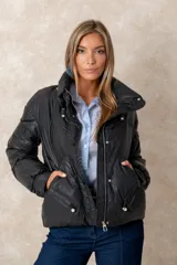 Campera puffer negra de acabado satinado con cuello alto ajustable, cierre frontal y bolsillos laterales. Presenta detalles de perlas en los cordones del cuello y del ruedo.