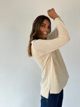 Buzo de tejido de punto ligero, color dorado con brillo sutil, escote en V y manga larga con diseño calado en los puños.