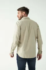 Camisa de hombre color beige con efecto stone wash, corte regular, cuello clásico, cierre frontal con botones, dos bolsillos con solapa abotonada en el pecho y mangas largas con puños abotonados.