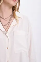 Camisa blanca de lino de manga larga con cuello clásico, cierre frontal con botones y bolsillo en el pecho.