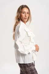 Camisa de gasa color blanco con volados frontales y en las mangas, cuello con lazo y mangas largas abullonadas con puños ajustados.