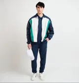 Campera deportiva Ellesse modelo Sako, diseño en bloques de color azul marino, blanco y verde, con cierre frontal completo, cuello alto y detalles de líneas blancas en las mangas.