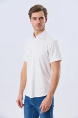 Camisa de manga corta confeccionada en tejido piqué de algodón, color blanco, con cuello con botones y cierre frontal abotonado.