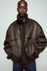Chaqueta bomber de cuello alto con forro interior de pelo sintético. Presenta cierre frontal con botones, bolsillos delanteros y bajo ajustable con cordones.