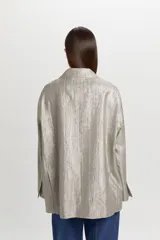 Blazer de corte oversize y estilo masculino, confeccionado en tejido con brillo metalizado y sutil patrón de rayas. Presenta solapas de muesca, cierre frontal de dos botones y bolsillos con solapa en los laterales.