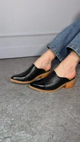 Zueco de cuero negro con punta cerrada lisa, cuerpo calado y tacón ancho de madera.