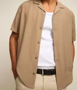 Pantalón de vestir color marrón, de corte slim y largo cropped. Confeccionado en tejido de algodón liso, con bolsillos laterales y traseros. Cierre frontal con botón y cremallera.