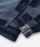 Campera de jacquard de algodón con diseño patchwork de cuadros en tonos azules. Presenta cuello inglés, cierre frontal con botones metálicos, mangas largas y bolsillos delanteros.