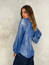 Blusa de manga larga color azul eléctrico con acabado brillante o metalizado, cuello alto y corte holgado.