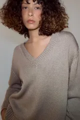 Sweater de punto grueso color beige, con cuello en V profundo y mangas largas. Cuenta con terminaciones acanaladas en el cuello, los puños y el ruedo.