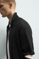 Camisa relaxed fit de punto tejida en hilatura con mezcla de algodón, color negro, con cuello solapa, manga corta y cierre frontal de botonadura.