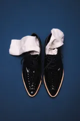 Zapato acordonado de cuero charol negro con detalle de trenzado en la puntera y suela color beige.