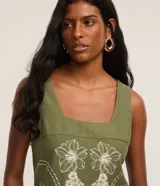 Vestido corto color verde militar con escote cuadrado, breteles anchos y sin mangas. Presenta un diseño estampado floral en color blanco de estilo simétrico y detalle de cenefa en el ruedo.