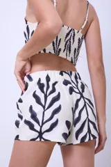 Top corto de lino color crudo con estampado de hojas en negro, breteles finos regulables y elástico en la espalda.