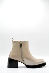 Bota corta de cuero en tono beige, con diseño bicolor que presenta un panel lateral en un tono más claro. Cuenta con un taco cuadrado negro de altura media y cierre lateral interno.