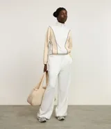 Campera deportiva de cuello alto con cierre frontal completo. Presenta un diseño bicolor en blanco y beige con líneas curvas en negro que definen la silueta. Confeccionada en una mezcla de poliéster, modal y elastano.