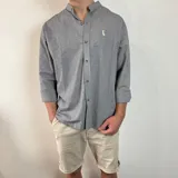 Camisa de algodón con cuello mao y estampado de rayas verticales finas. Presenta cierre frontal con botones y logo bordado en el pecho.