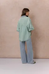 Camisa lila de calce relajado y manga larga, con cuello clásico, puños y bolsillo delantero en denim contrastante. Cierre frontal con broches metálicos.