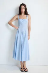 Vestido midi de color celeste con escote cuadrado y tirantes anchos. Presenta un diseño entallado en el torso con falda acampanada terminada en godets que aportan volumen y movimiento. Incluye cierre lateral con cremallera oculta.