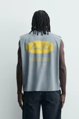 Musculosa de corte relajado con efecto lavado, cuello redondo y sisas amplias. Presenta estampados gráficos en color amarillo en el frente y acabados irregulares que le otorgan una apariencia única.