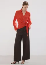 Camisa de viscosa y poliamida color rojo, con cuello camisero, manga larga y diseño cruzado con lazo ajustable en la cintura.