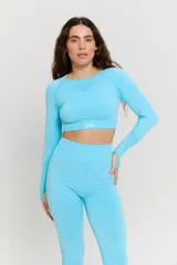 Conjunto deportivo de dos piezas color turquesa, compuesto por un top de manga larga con cuello redondo y detalle de textura en el pecho, y calzas de tiro alto. Ambas prendas presentan un diseño sin costuras con detalles texturizados y logo estampado en el top.