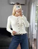 Saquito de tejido bremer color crema, con cuello redondo, cierre frontal de botones y detalles de volados en el ruedo y los puños.