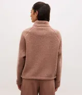 Campera bomber de mujer confeccionada en tejido sherpa color rosa viejo, con cuello alto, cierre frontal con cremallera y detalles de paneles lisos contrastantes en el pecho.