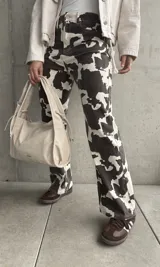 Pantalón de jean de corte recto con estampado de manchas de vaca en tonos marrón y blanco.